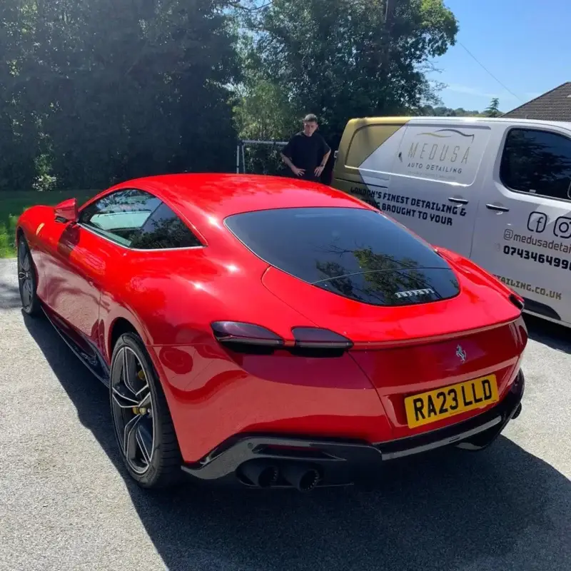 Rear view of a gleaming red Ferrari with RA23 LLD plate, freshly detailed by Medusa Auto Detailing, with branded van and detailer in background.